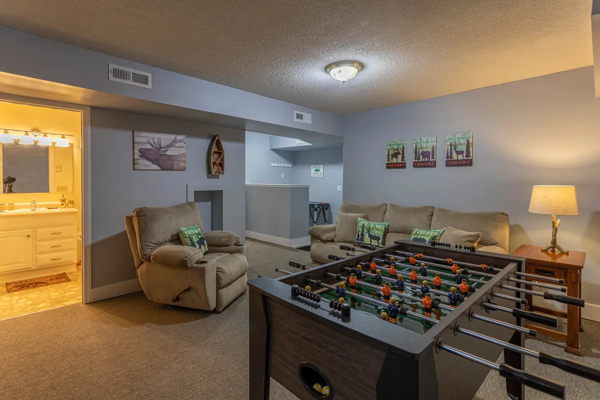 A vibrant game room featuring a foosball table set up for play, reclining chairs for comfortable viewing or relaxation, a welcoming lamp, and playful artwork adorning the walls. The space exudes a sense of fun and togetherness, inviting guests of all ages to enjoy games or unwind.