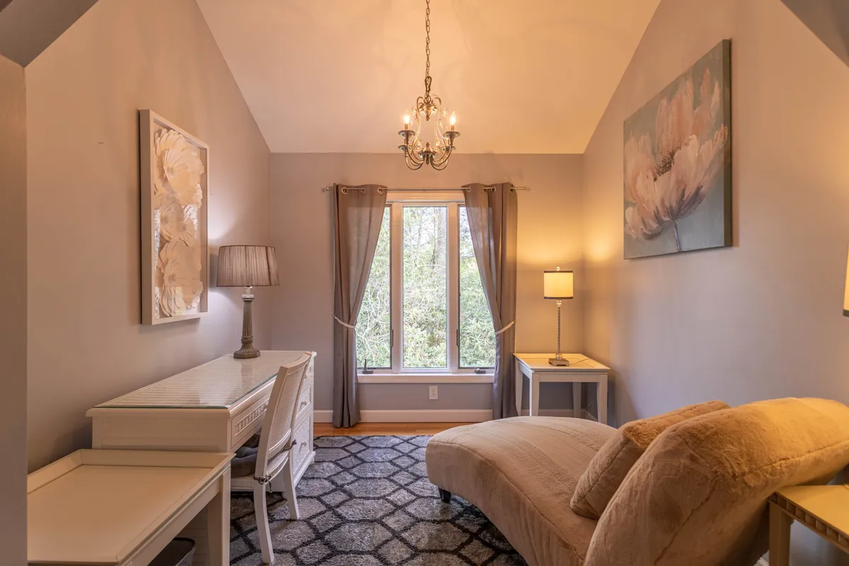 A tranquil, light-filled nook with a comfortable chaise lounge by a large window, chic chandelier, and decorative artwork. The window opens up to views of the outdoors, creating a perfect spot for reading or simply enjoying the peaceful surroundings.