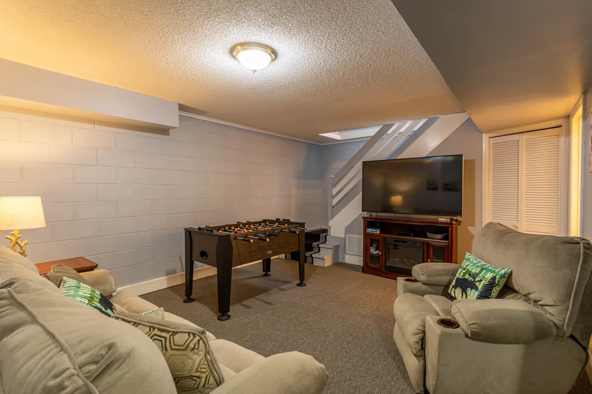 The interior game room highlights a foosball table, a large television, and a comfortable sofa, set up for both play and relaxation. The mood is friendly and casual, supporting active family engagement and entertainment options for all ages.