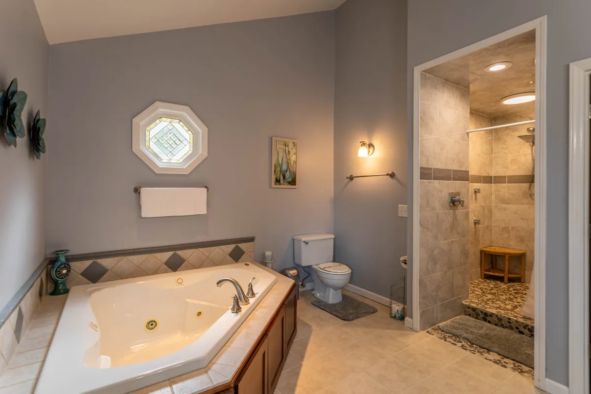 A luxurious master bathroom with a whirlpool soaking tub, an octagonal window providing natural light, a shower area, and decorative wall art. The scene feels tranquil and indulgent, perfect for relaxation and self-care.