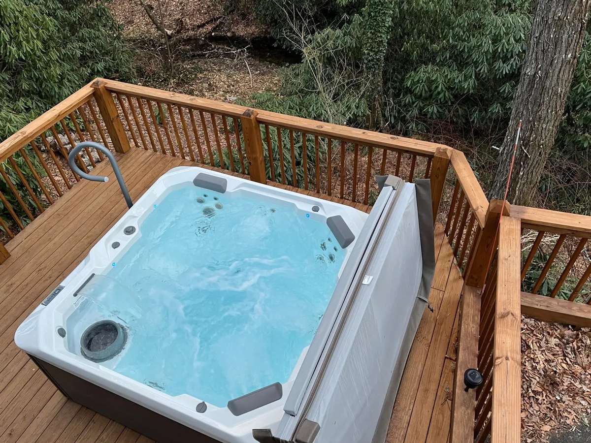 A tranquil exterior shot of a private hot tub positioned on a wooden deck, surrounded by greenery, setting the mood for serene soaks under the stars or peaceful moments with nature.