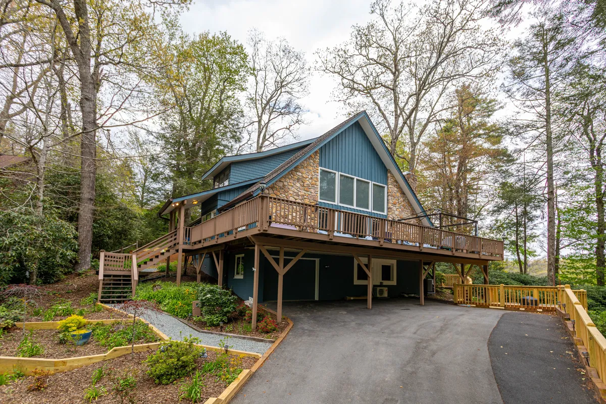 This exterior image features the iconic A-frame structure of the cabin, a spacious wooden deck, and lush surrounding greenery. The deck is set up for relaxing or outdoor gatherings, highlighting spaces where families can enjoy fresh mountain air and nature views together.