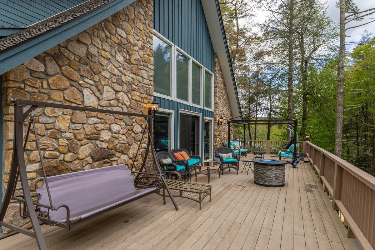 A welcoming outdoor deck with a stone wall, comfortable seating options, decorative accents, a cozy fire pit, and lush natural surroundings. The space is ideal for gathering, relaxing with coffee in the morning, or sharing stories by the fire table in the evening.